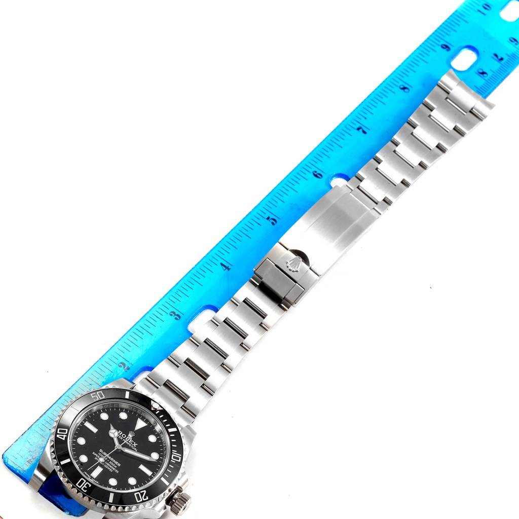 The image shows a Rolex Submariner 114060 Men
s Stainless Steel Black Dial 114060 Men
s Stainless Steel Black Dial watch lying flat with its bracelet extended, next to a blue ruler.