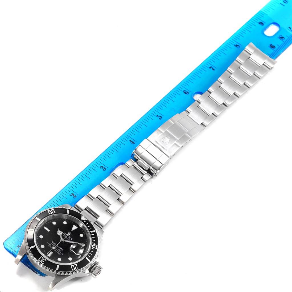 The watch, a Rolex Submariner 16610 Men
s Stainless Steel Black Dial 16610 Men
s Stainless Steel Black Dial, is shown from a top-down angle alongside a ruler, displaying its bracelet and clasp.