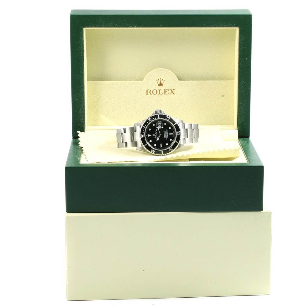 The image shows a Rolex Submariner 16610 Men
s Stainless Steel Black Dial 16610 Men
s Stainless Steel Black Dial displayed inside an open green and cream-colored Rolex box.