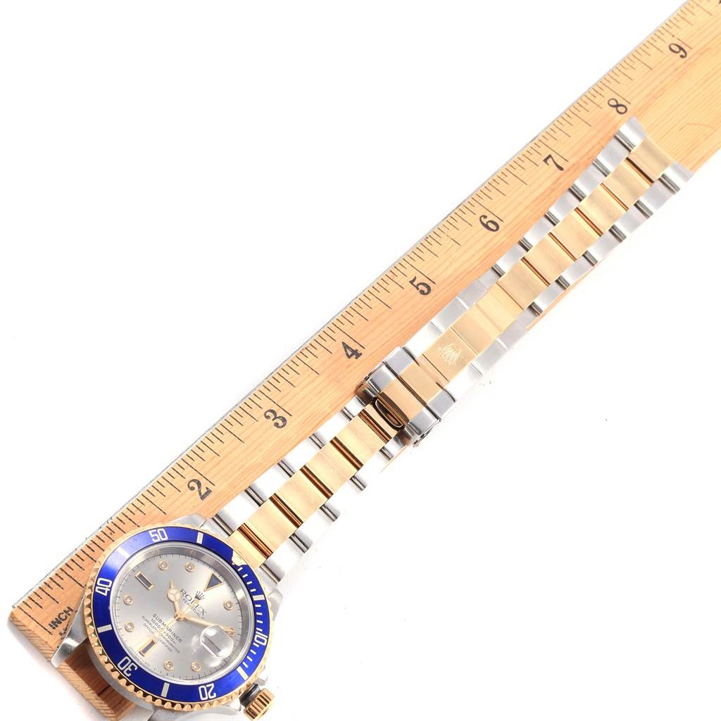 The angle shows the full length of the Rolex Submariner 16613 Men
s Steel and Gold (two tone) Grey Dial 16613 Men
s Steel and Gold (two tone) Grey Dial watch, with the face and bracelet laid next to a ruler.