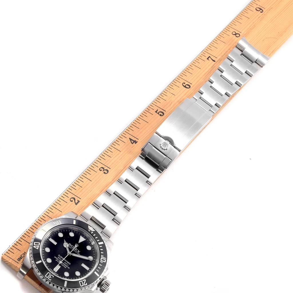 The image shows a Rolex Submariner 114060 Men
s Stainless Steel Black Dial 114060 Men
s Stainless Steel Black Dial model watch and its stainless steel bracelet laid next to a wooden ruler.