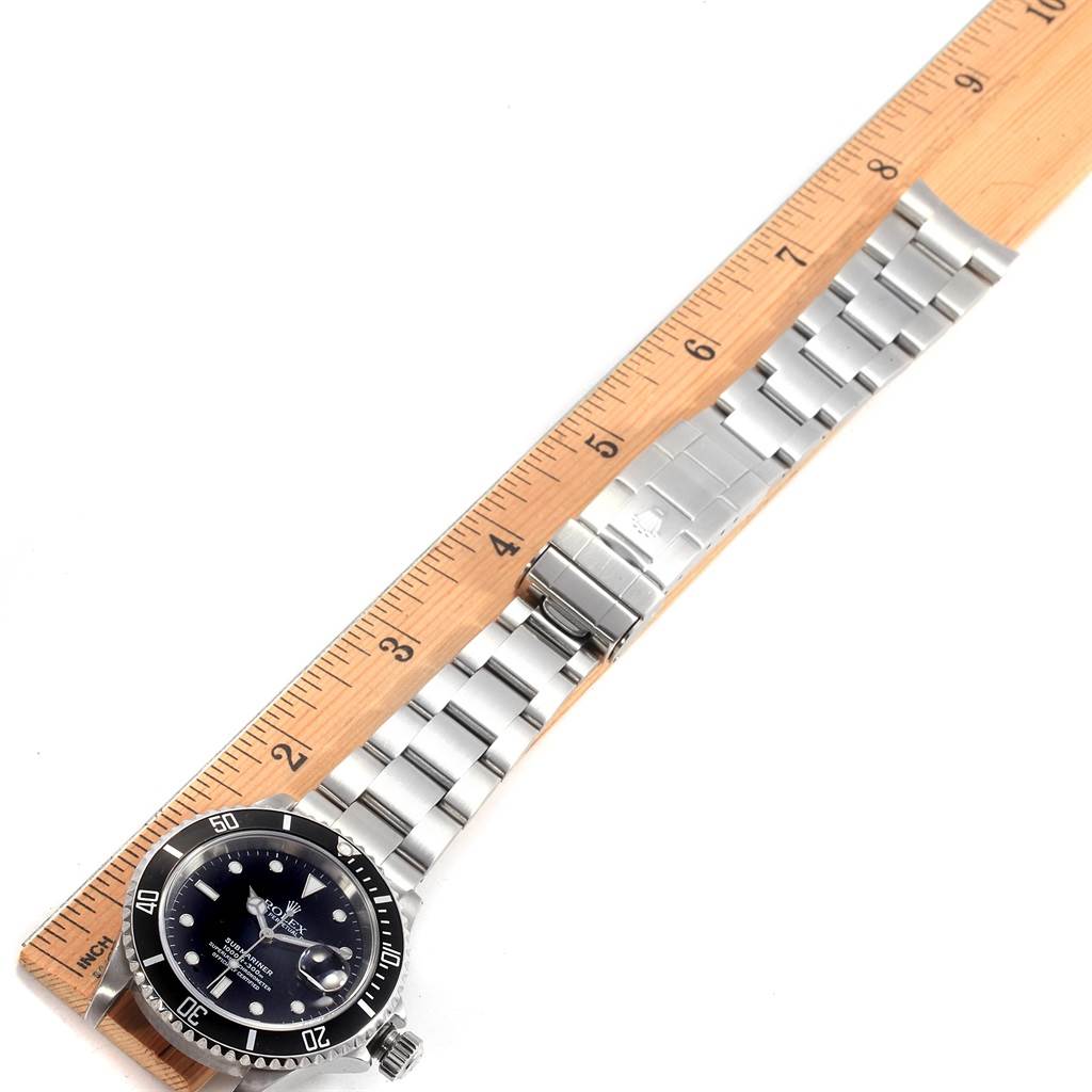 The image shows a top view of a Rolex Submariner 16610 Men
s Stainless Steel Black Dial 16610 Men
s Stainless Steel Black Dial watch with its face and metal strap placed next to a ruler.