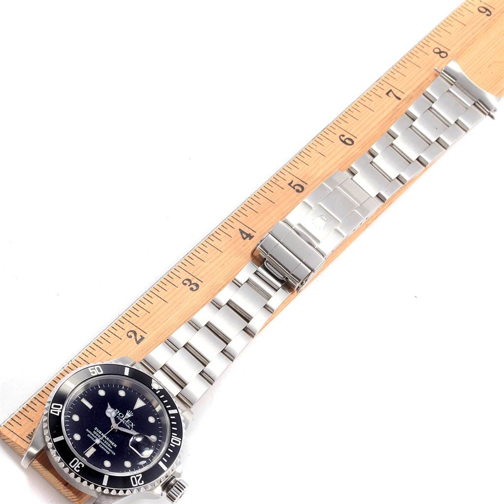 The Rolex Submariner 16610 Men
s Stainless Steel Black Dial 16610 Men
s Stainless Steel Black Dial watch is shown from a top-down angle with its stainless steel bracelet and a wooden ruler for scale.