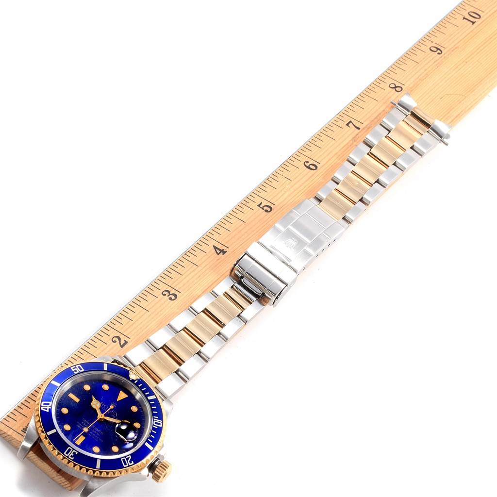 The Rolex Submariner 16613 Men's Steel and Gold (two tone) Blue Dial 16613 Men's Steel and Gold (two tone) Blue Dial watch is shown fully extended, aligned next to a ruler displaying its bracelet and face.