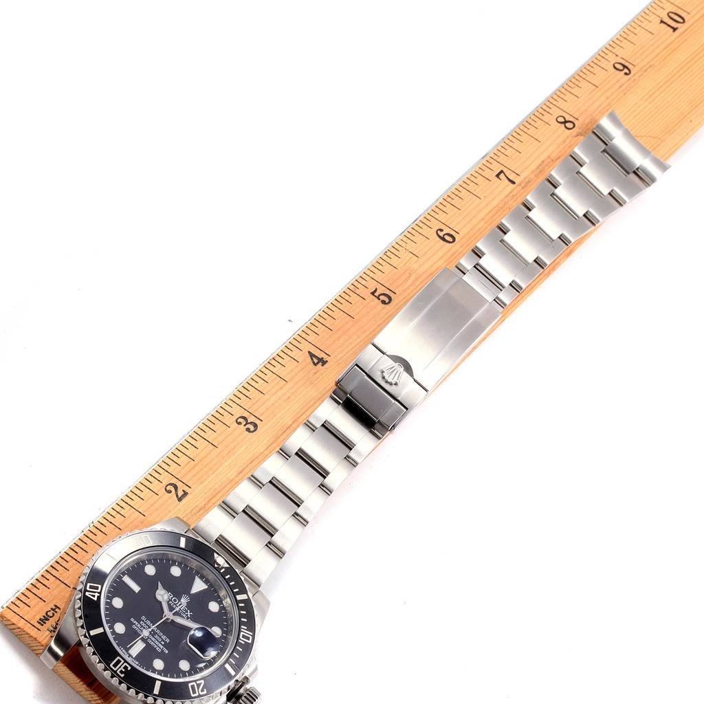The image shows a side angle of a Rolex Submariner 116610 Men
s Stainless Steel Black Dial 116610 Men
s Stainless Steel Black Dial watch, highlighting its stainless steel bracelet and clasp, alongside a measurement ruler.