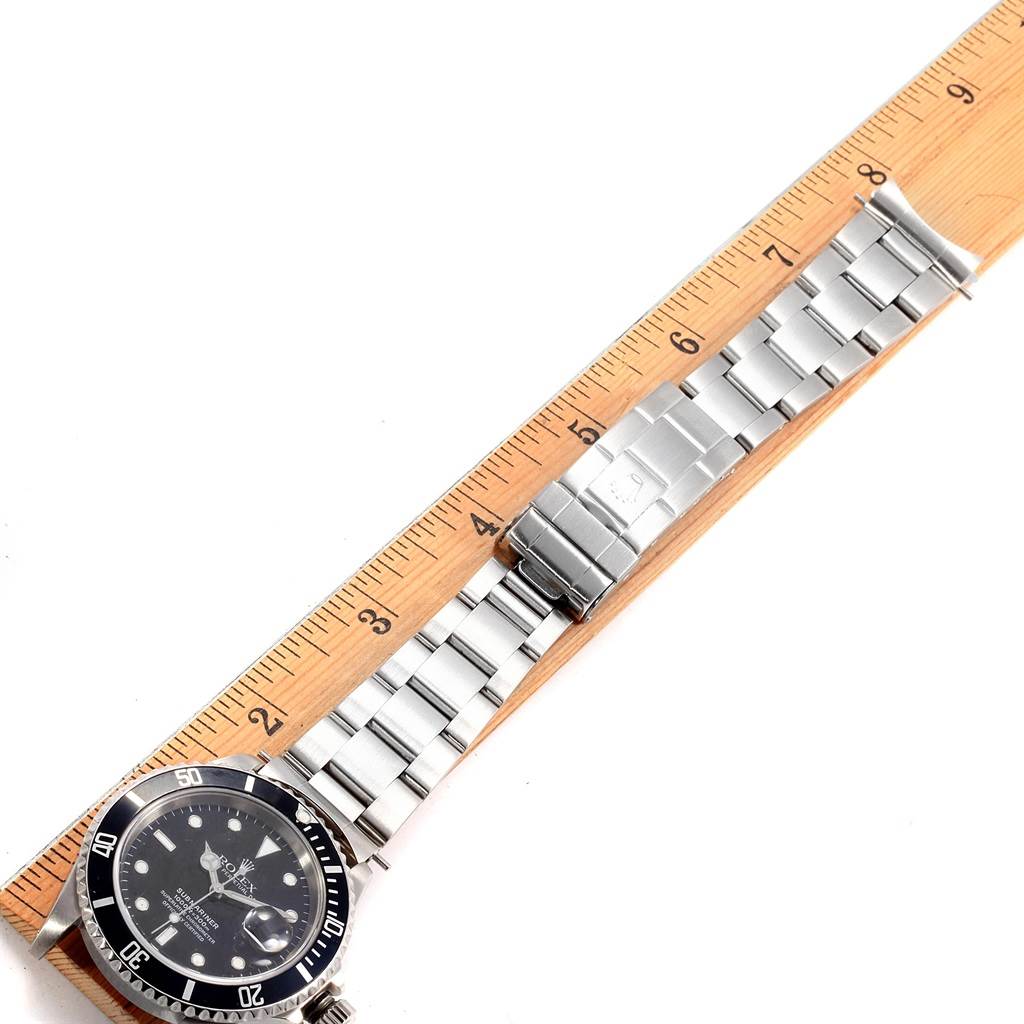 This image shows a Rolex Submariner 16610 Men
s Stainless Steel Black Dial 16610 Men
s Stainless Steel Black Dial watch laid flat next to a ruler, with the face, bezel, bracelet, and clasp fully visible.