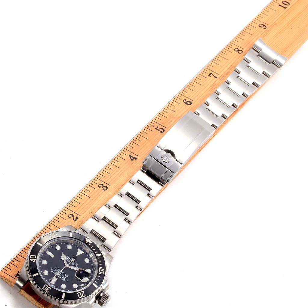The image shows the Rolex Submariner 116610 Men
s Stainless Steel Black Dial 116610 Men
s Stainless Steel Black Dial watch laid flat against a ruler, displaying its face, bracelet, and clasp.