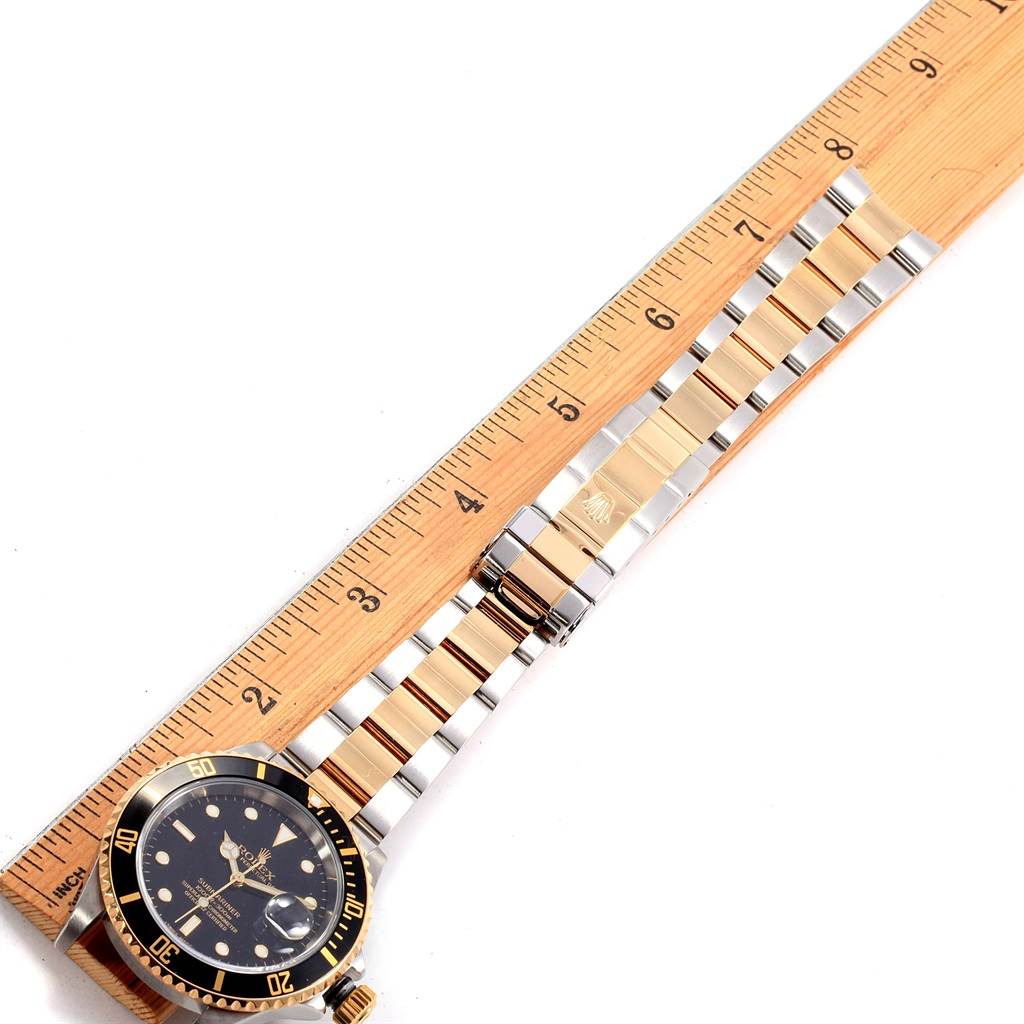 The image shows a Rolex Submariner 16613 Men's Steel and Gold (two tone) Black Dial 16613 Men's Steel and Gold (two tone) Black Dial watch laid flat next to a ruler, highlighting the bezel, dial, and bracelet.