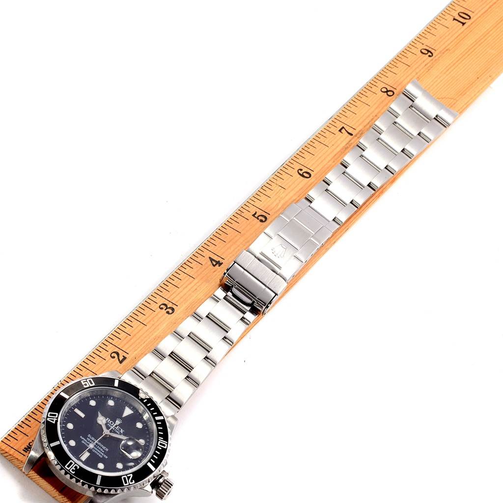 The Rolex Submariner 16610 Men
s Stainless Steel Black Dial 16610 Men
s Stainless Steel Black Dial watch is displayed face-up, showing the full watch and the metal bracelet next to a ruler for scale.