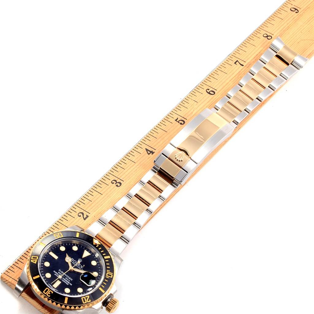The image shows the Rolex Submariner 116613 Men's Steel and Gold (two tone) Black Dial 116613 Men's Steel and Gold (two tone) Black Dial watch placed on a ruler, displaying its front face, bracelet, and clasp.