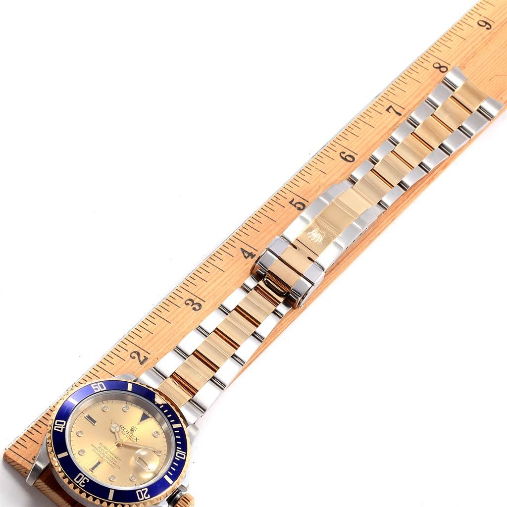 This image shows a Rolex Submariner 16613 Men
s Steel and Gold (two tone) Champagne Dial 16613 Men
s Steel and Gold (two tone) Champagne Dial watch laid flat on a ruler, highlighting its band, bezel, and face from a top-down angle.