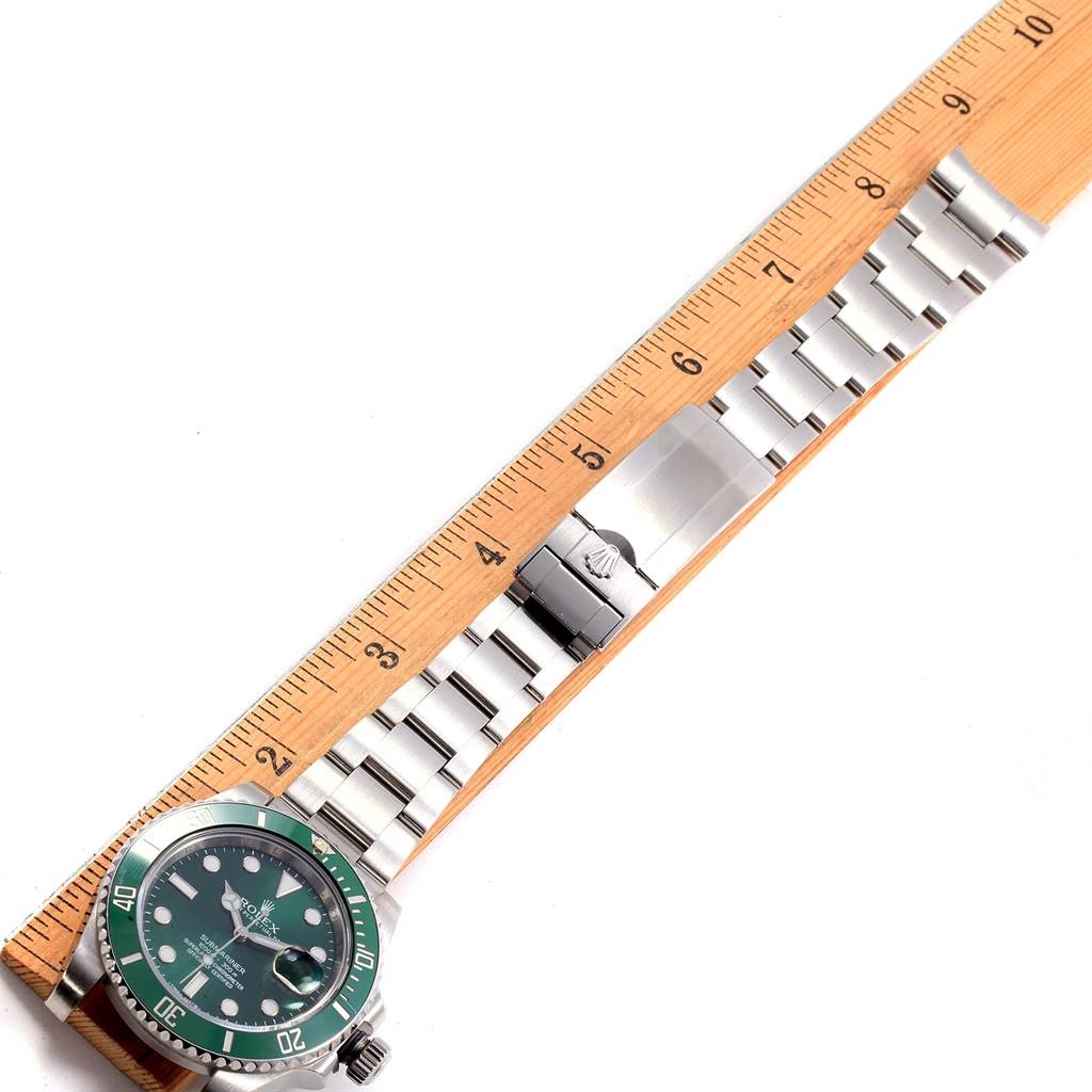 The image shows a side angle of a Rolex Submariner 116610LV Men
s Stainless Steel Green Dial 116610LV Men
s Stainless Steel Green Dial watch with a green dial and a stainless steel bracelet aligned next to a ruler.