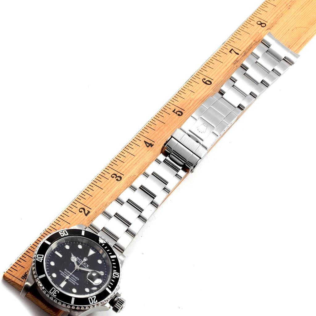 The image shows a top-down view of a Rolex Submariner 16610 Men
s Stainless Steel Black Dial 16610 Men
s Stainless Steel Black Dial watch and its metal bracelet with a ruler for measurement.