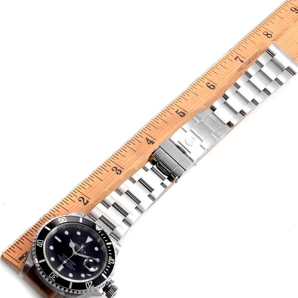 The image shows a side view of a Rolex Submariner 16610 Men
s Stainless Steel Black Dial 16610 Men
s Stainless Steel Black Dial watch, focusing on the face, bezel, and stainless steel bracelet with a ruler for scale.