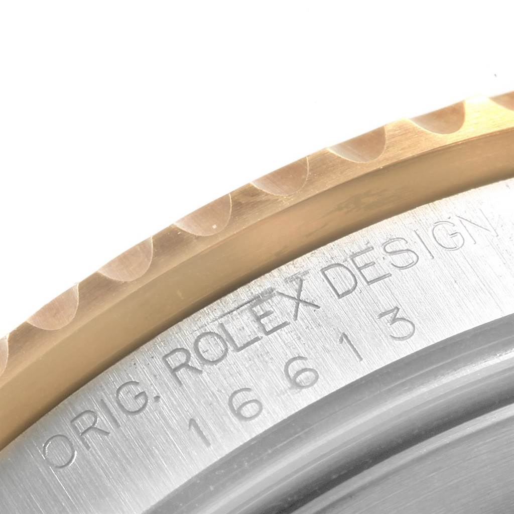 The image shows a close-up angle of the bezel and casing of a Rolex Submariner 16613 Men's Steel and Gold (two tone) Grey Dial 16613 Men's Steel and Gold (two tone) Grey Dial, displaying engraved text.