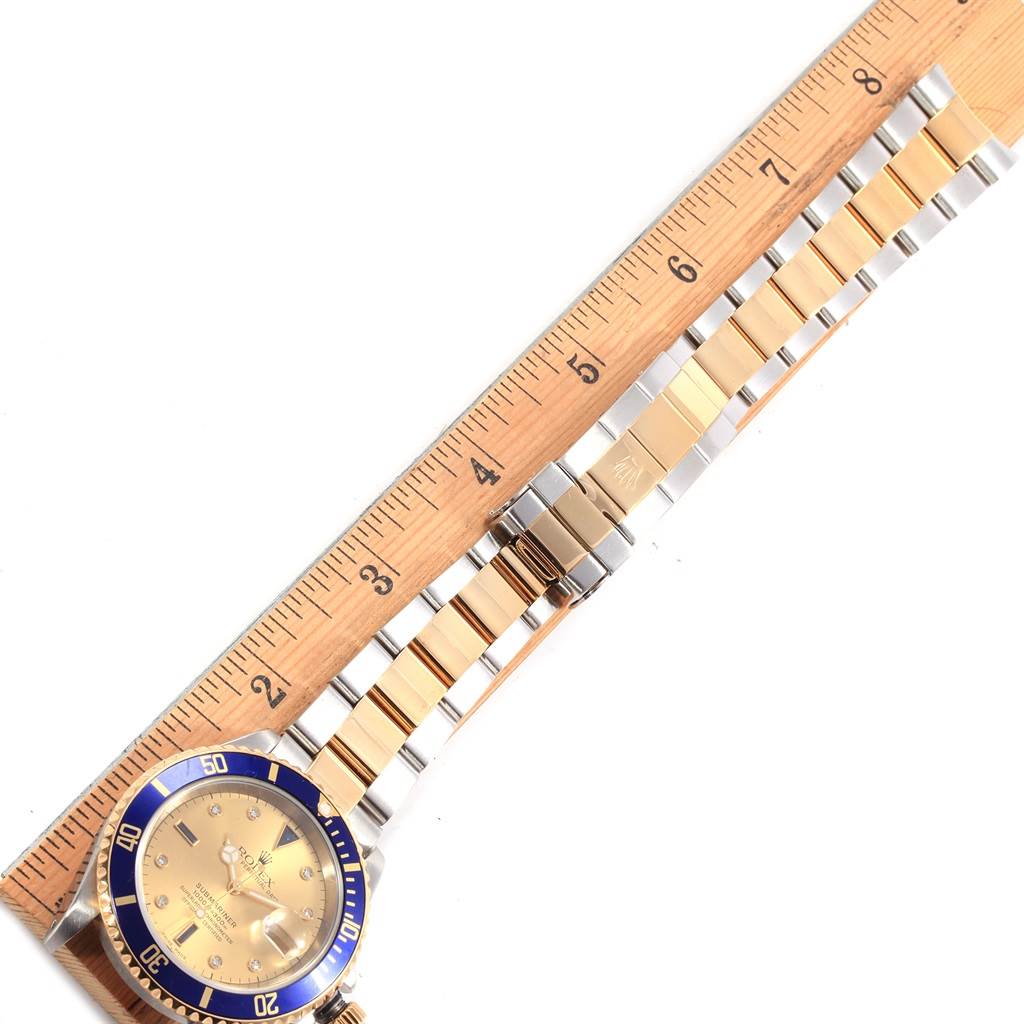 The image displays a Rolex Submariner 16613 Men's Steel and Gold (two tone) Champagne Dial 16613 Men's Steel and Gold (two tone) Champagne Dial watch laid flat, showing the face, bezel, and part of the bracelet alongside a ruler.