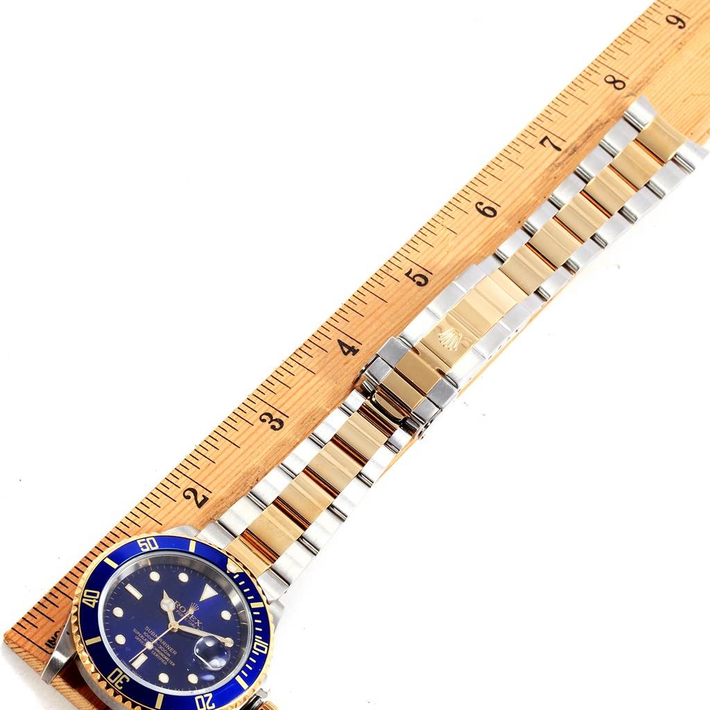 The Rolex Submariner 16613 Men's Steel and Gold (two tone) Blue Dial 16613 Men's Steel and Gold (two tone) Blue Dial watch is shown with its bracelet laid flat next to a ruler for measurement.