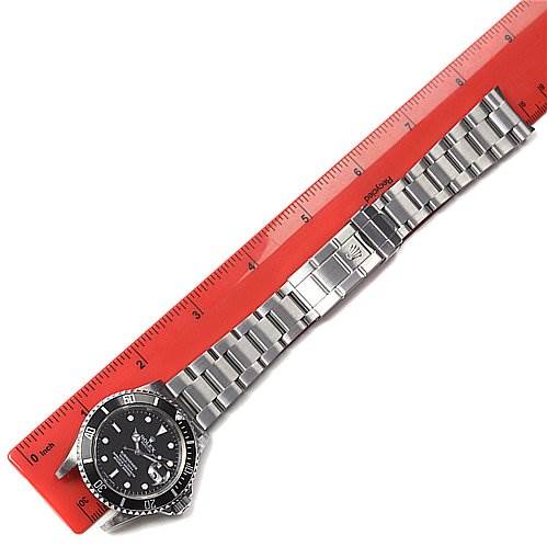 The Rolex Submariner 16610 Men's Stainless Steel Black Dial 16610 Men's Stainless Steel Black Dial watch is shown at a slight angle with its stainless steel bracelet fully extended alongside a ruler.