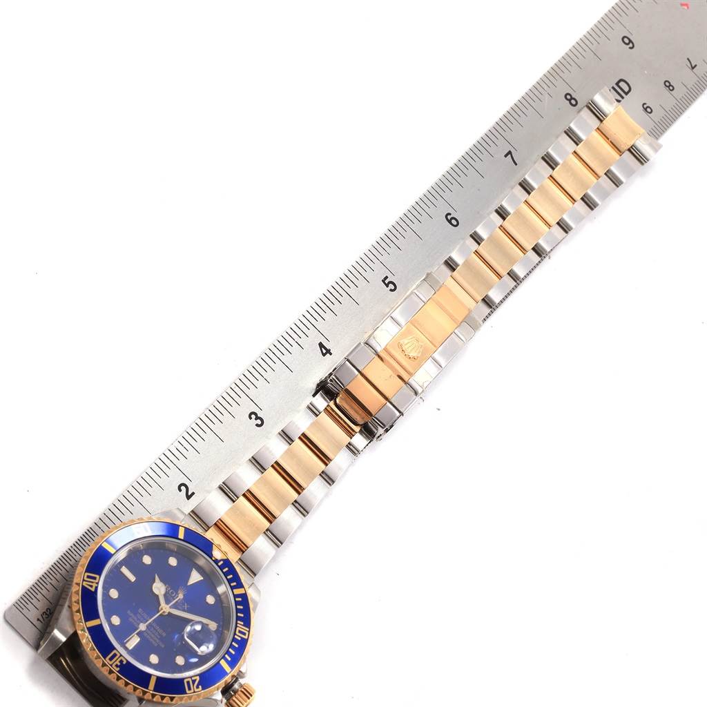The image shows a Rolex Submariner 16613 Men's Steel and Gold (two tone) Blue Dial 16613 Men's Steel and Gold (two tone) Blue Dial watch with a blue dial, gold bezel, and a two-tone metal bracelet beside a ruler for measurement.