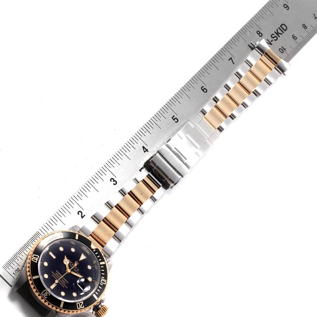 The image shows a top view of a Rolex Submariner 16613 Men's Steel and Gold (two tone) Black Dial 16613 Men's Steel and Gold (two tone) Black Dial watch, featuring the face, bezel, and bracelet next to a ruler.