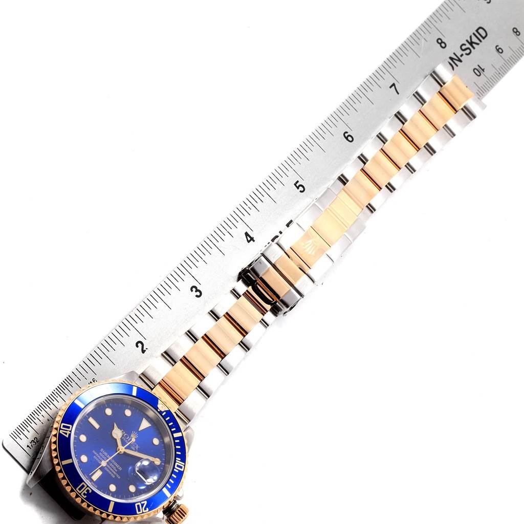 The image shows a top-down view of a Rolex Submariner 16613 Men's Steel and Gold (two tone) Blue Dial 16613 Men's Steel and Gold (two tone) Blue Dial watch, including its blue dial, bezel, and two-tone metal bracelet, with a ruler placed alongside.
