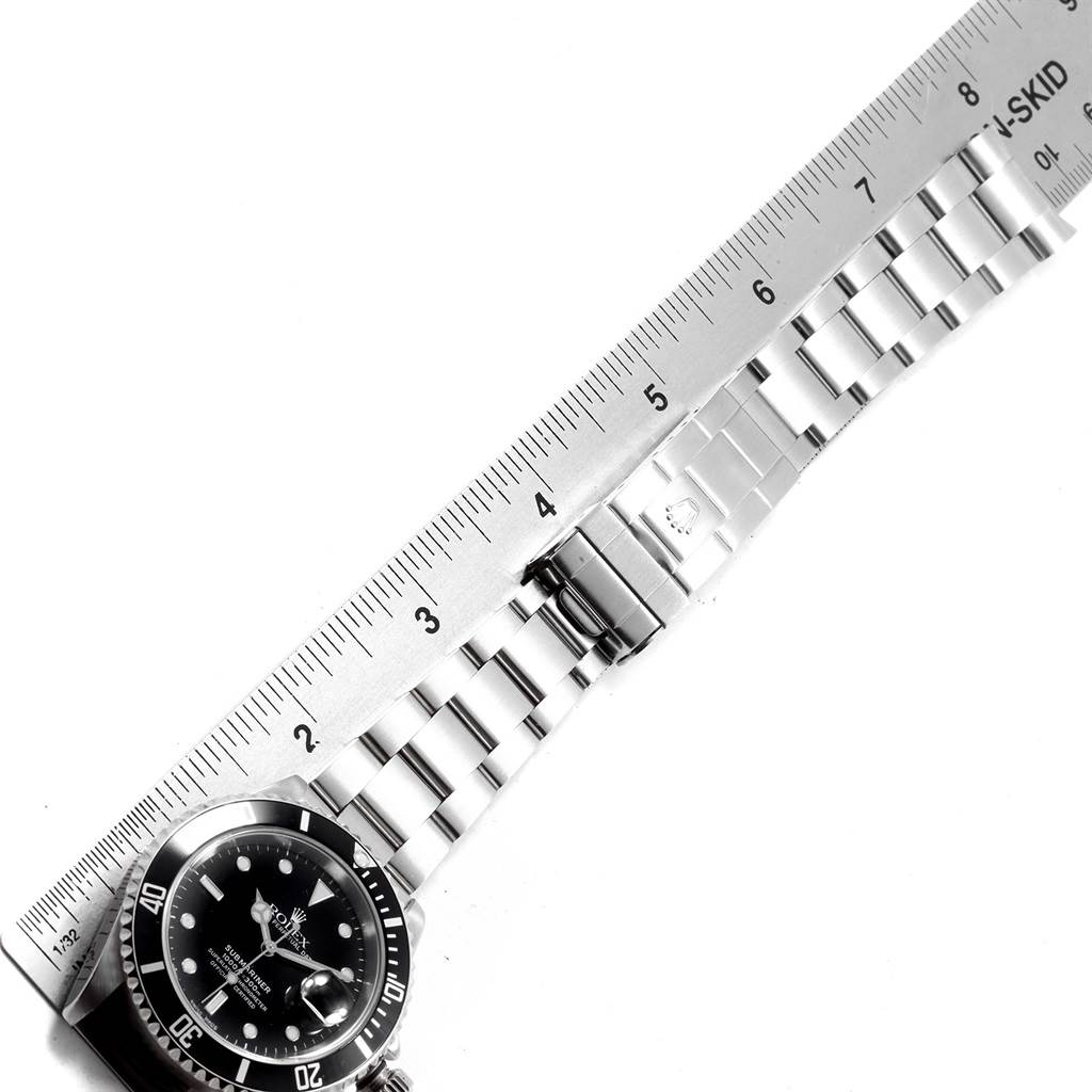 The Rolex Submariner 16610 Men
s Stainless Steel Black Dial 16610 Men
s Stainless Steel Black Dial watch is photographed from the top, showing its face, bezel, and metal bracelet next to a ruler.