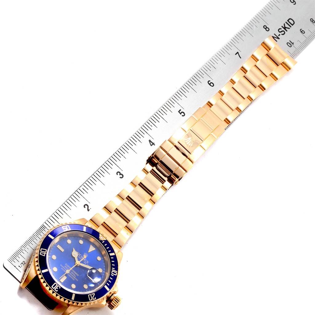 The image shows a Rolex Submariner 16618 Men's Yellow Gold Blue Dial 16618 Men's Yellow Gold Blue Dial watch laid flat with its full bracelet and clasp visible, alongside a ruler.
