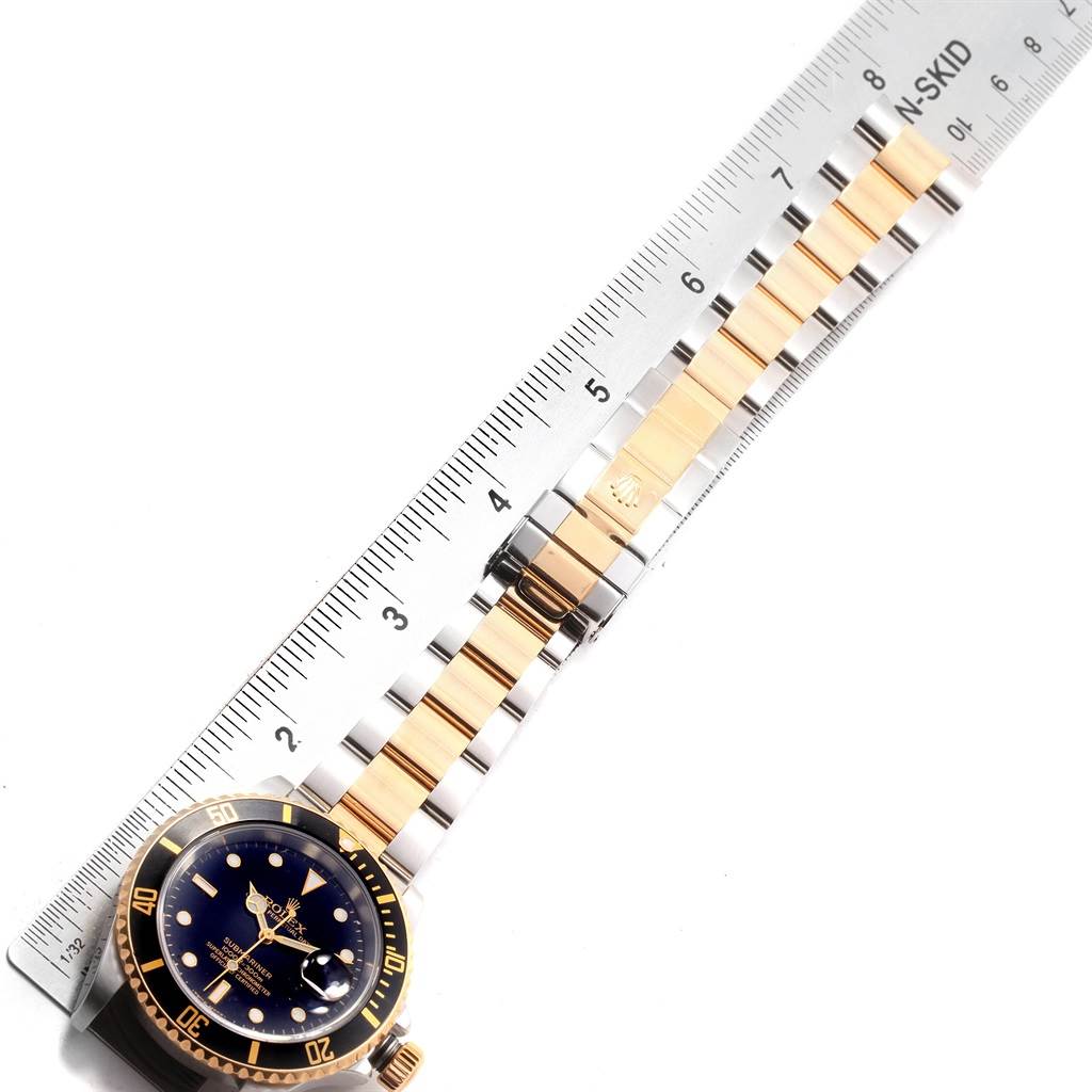 This image shows a Rolex Submariner 16613 Men's Steel and Gold (two tone) Black Dial 16613 Men's Steel and Gold (two tone) Black Dial watch laid flat with a ruler beneath, displaying the bracelet and face at a straight angle.