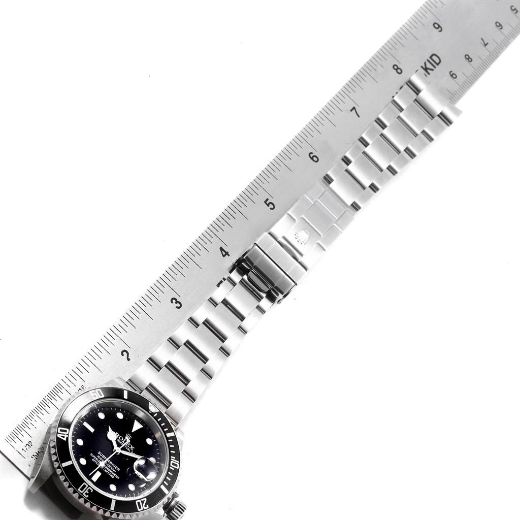 The image shows a Rolex Submariner 16610 Men's Stainless Steel Black Dial 16610 Men's Stainless Steel Black Dial watch face and part of its metal bracelet alongside a ruler.