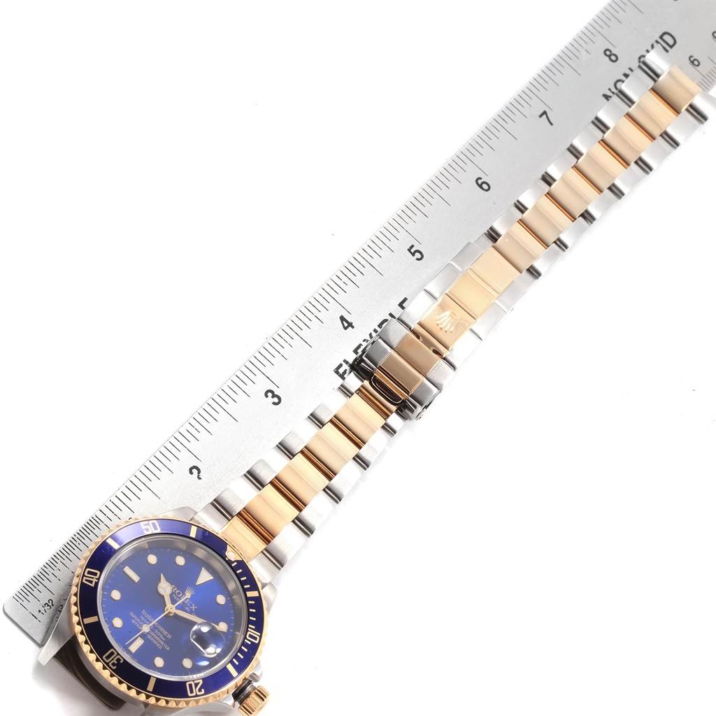 The image shows a top-down view of a Rolex Submariner 16613 Men's Steel and Gold (two tone) Blue Dial 16613 Men's Steel and Gold (two tone) Blue Dial watch with a two-tone stainless steel and gold bracelet, next to a ruler.