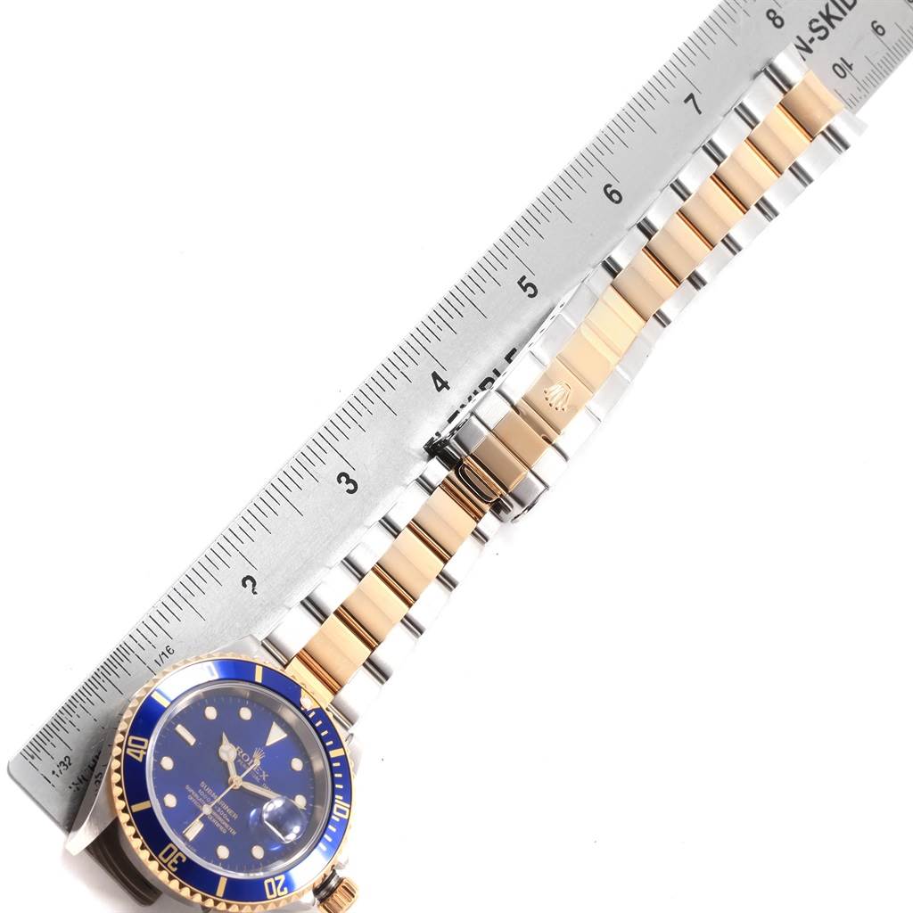 The image shows a Rolex Submariner 16613 Men's Steel and Gold (two tone) Blue Dial 16613 Men's Steel and Gold (two tone) Blue Dial watch laid flat with a ruler alongside it, showing the band and watch face.