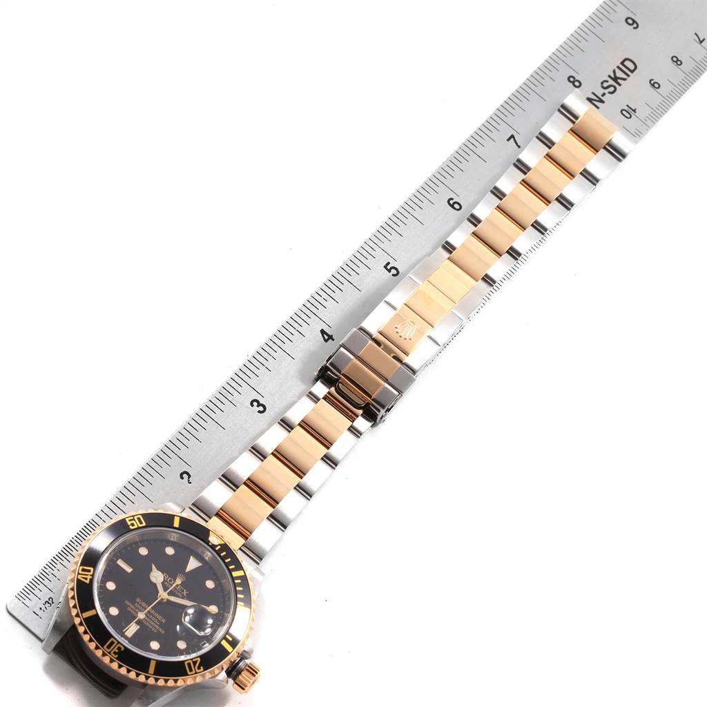 The image shows a Rolex Submariner 16613 Men's Steel and Gold (two tone) Black Dial 16613 Men's Steel and Gold (two tone) Black Dial watch from a top-down angle, highlighting its face, bezel, and two-tone bracelet adjacent to a ruler.