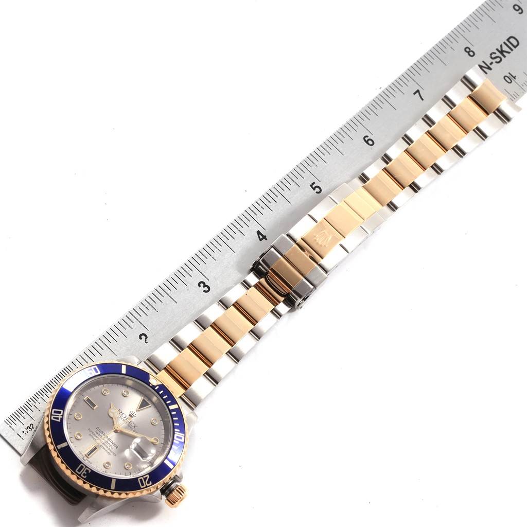 This image shows a Rolex Submariner 16613 Men's Steel and Gold (two tone) Grey Dial 16613 Men's Steel and Gold (two tone) Grey Dial watch laid flat next to a ruler, displaying the watch face and full bracelet.