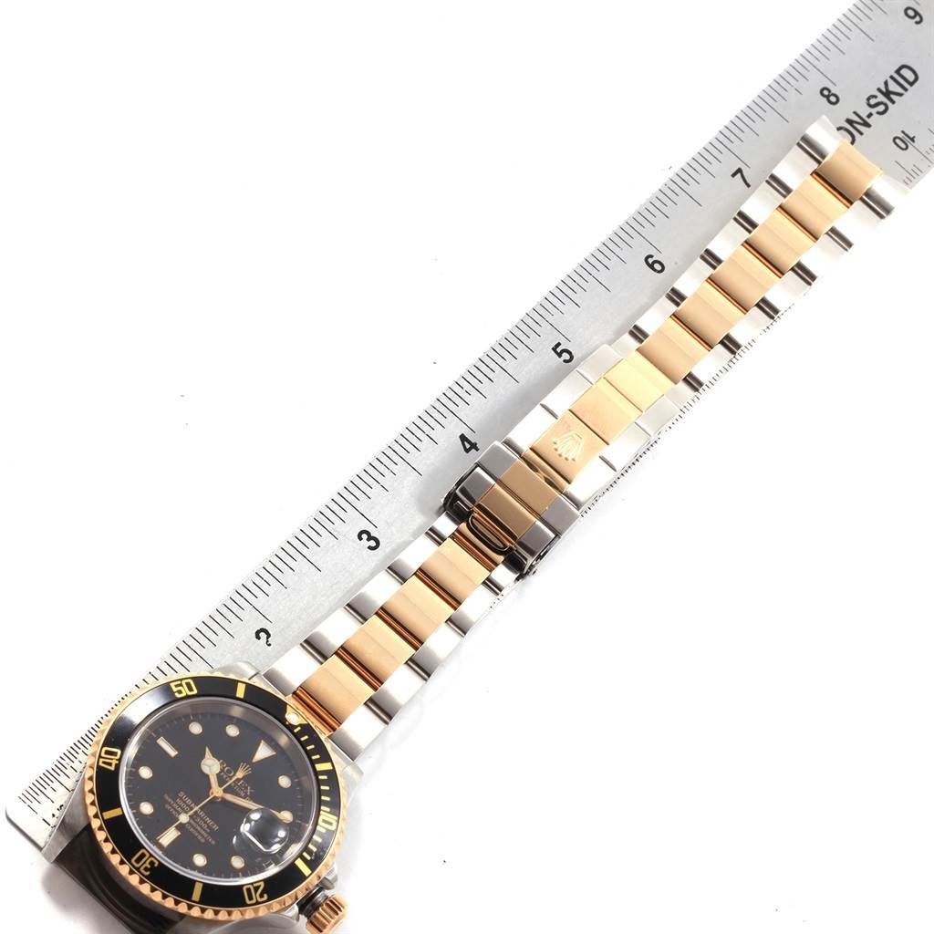 The image shows a Rolex Submariner 16613 Men's Steel and Gold (two tone) Black Dial 16613 Men's Steel and Gold (two tone) Black Dial watch laid flat with a focus on its two-tone bracelet and ruler for size measurement.