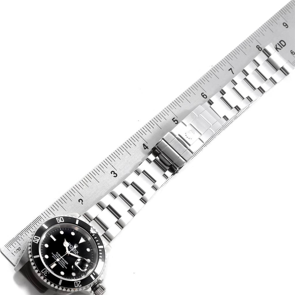 The image shows a top-down view of a Rolex Submariner 16610 Men's Stainless Steel Black Dial 16610 Men's Stainless Steel Black Dial watch, including the face, bezel, and band, beside a ruler.
