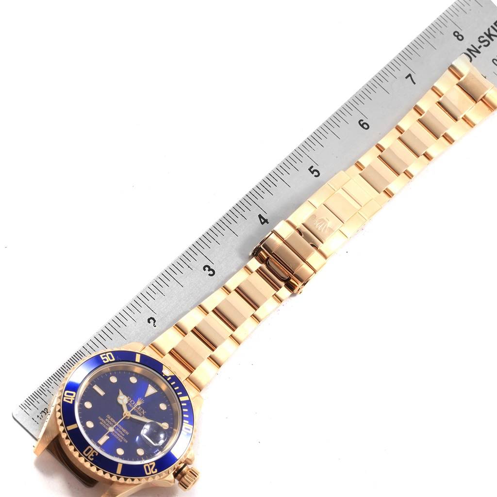 The image shows a top-down view of a Rolex Submariner 16618 Men's Yellow Gold Blue Dial 16618 Men's Yellow Gold Blue Dial watch with a blue bezel and gold bracelet next to a ruler for scale.