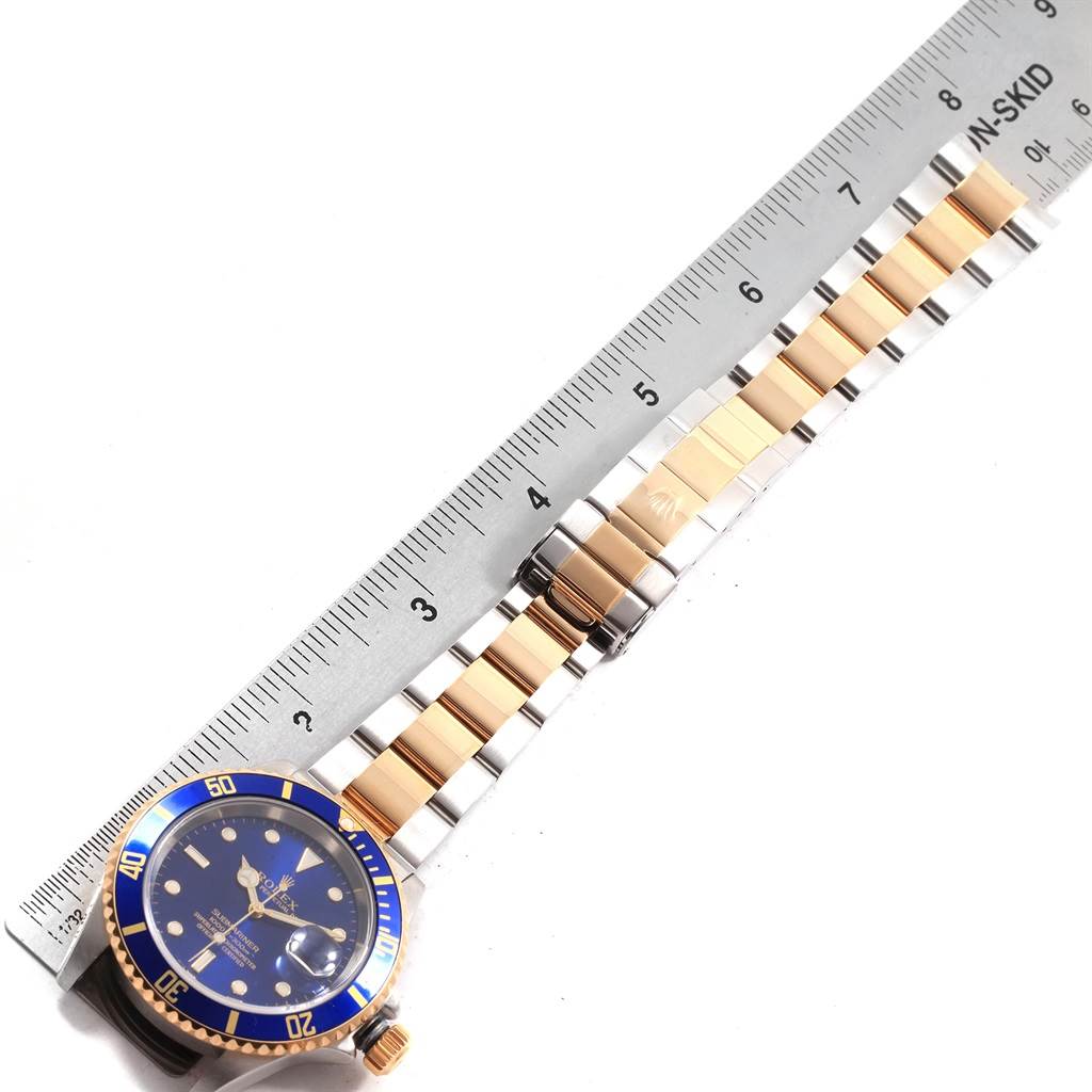The image shows a top-down view of a Rolex Submariner 16613 Men's Steel and Gold (two tone) Blue Dial 16613 Men's Steel and Gold (two tone) Blue Dial watch, highlighting its bracelet, bezel, and case with a ruler for scale.