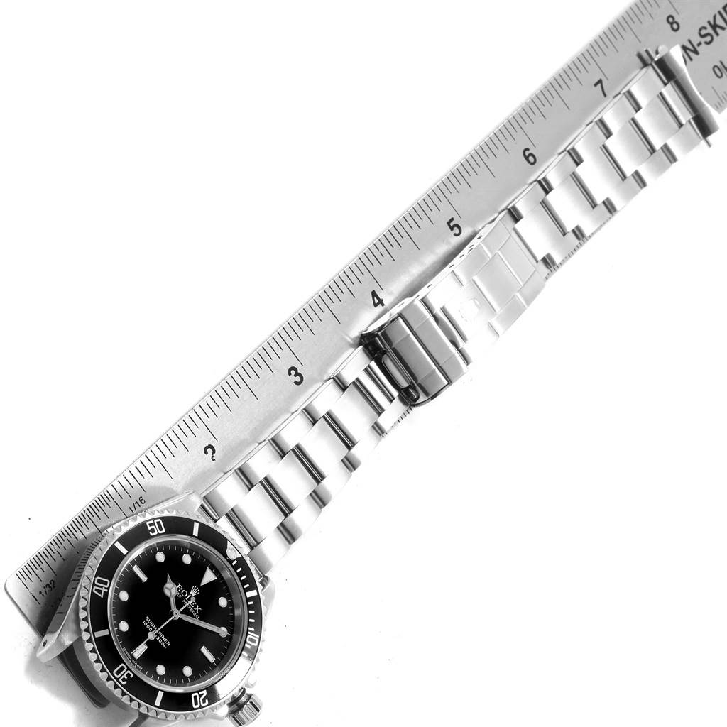 This image shows the face and bracelet of a Rolex Submariner 14060 Men's Stainless Steel Black Dial 14060 Men's Stainless Steel Black Dial watch, with the bracelet laid next to a ruler.