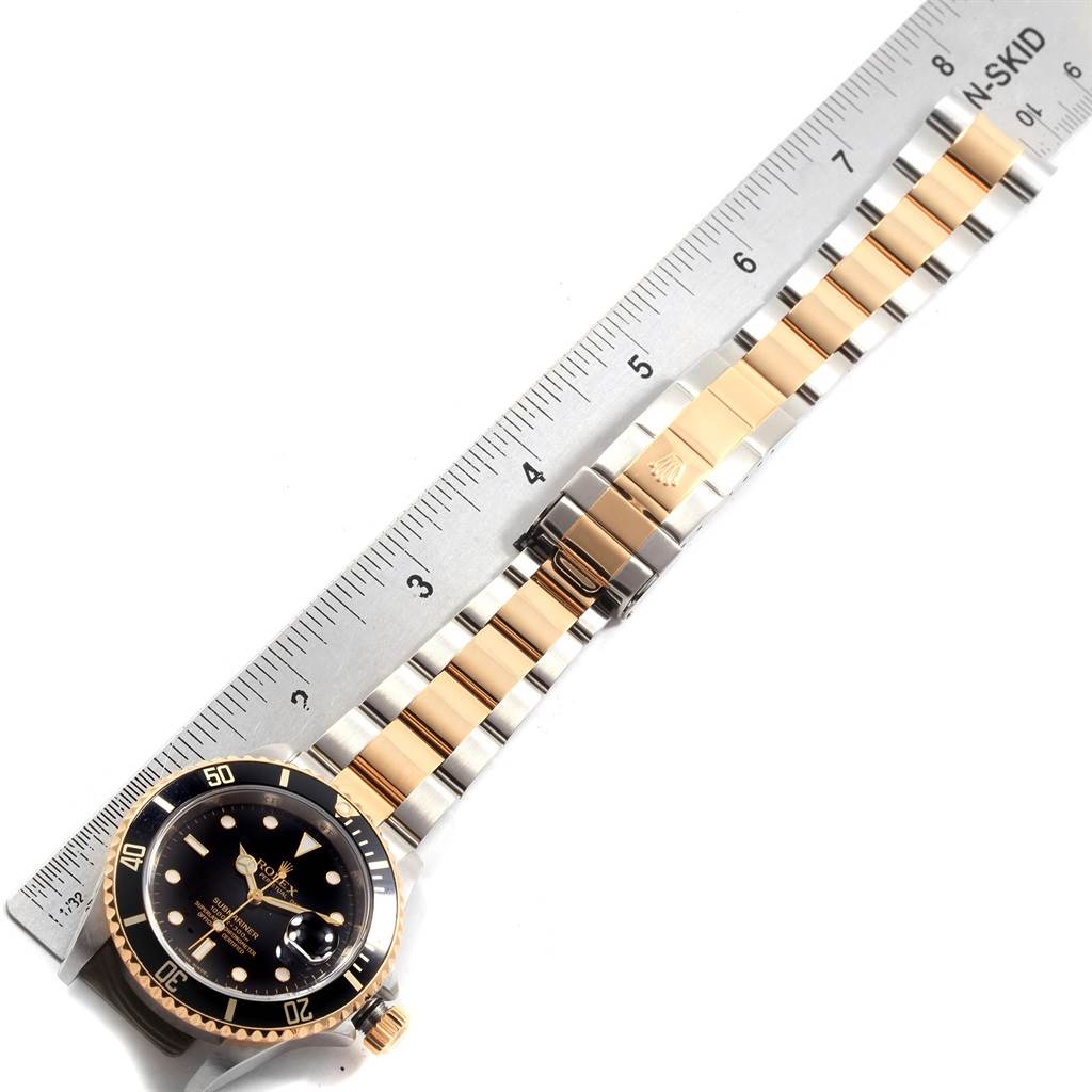 The image shows the Rolex Submariner 16613 Men's Steel and Gold (two tone) Black Dial 16613 Men's Steel and Gold (two tone) Black Dial watch laid flat with its bracelet extended alongside a ruler for measurement.