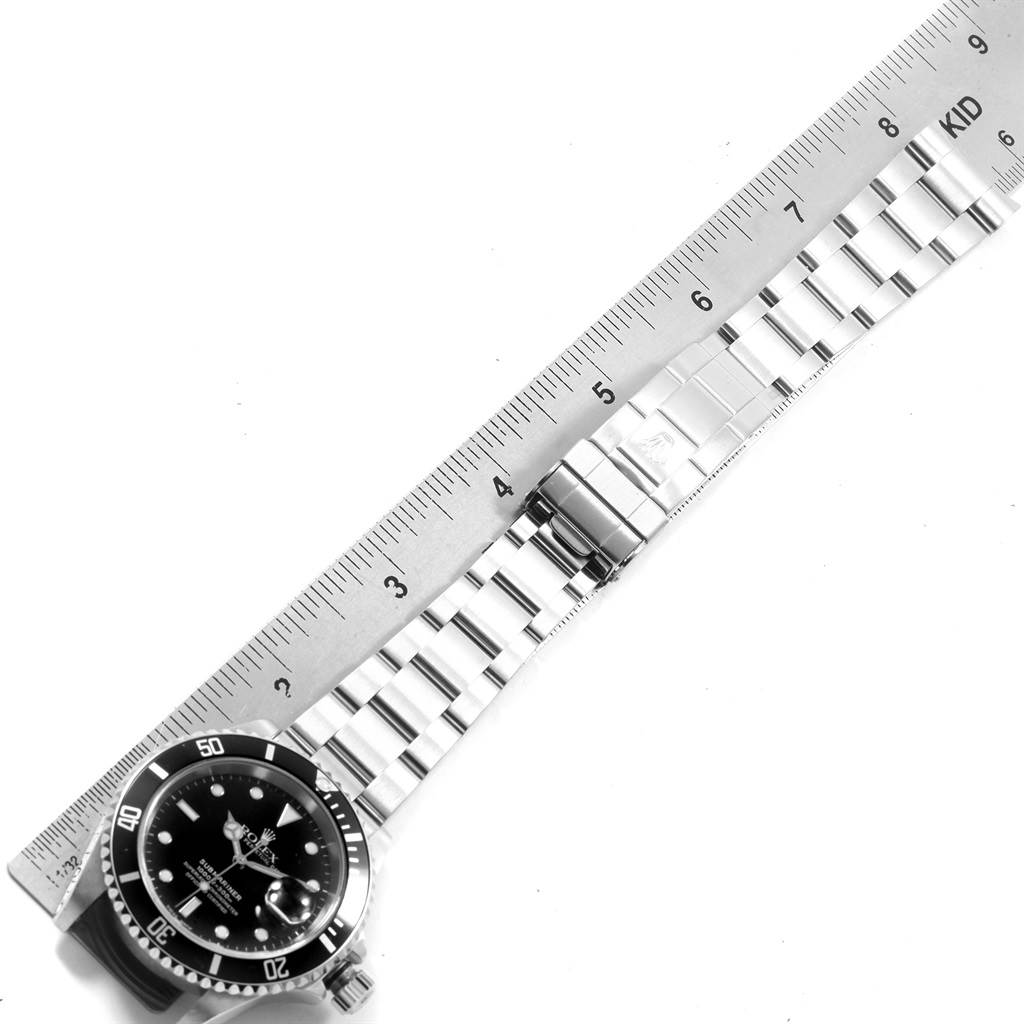 The image shows the Rolex Submariner 16610 Men's Stainless Steel Black Dial 16610 Men's Stainless Steel Black Dial watch laid flat, with a focus on its bracelet and clasp, alongside a ruler for scale.