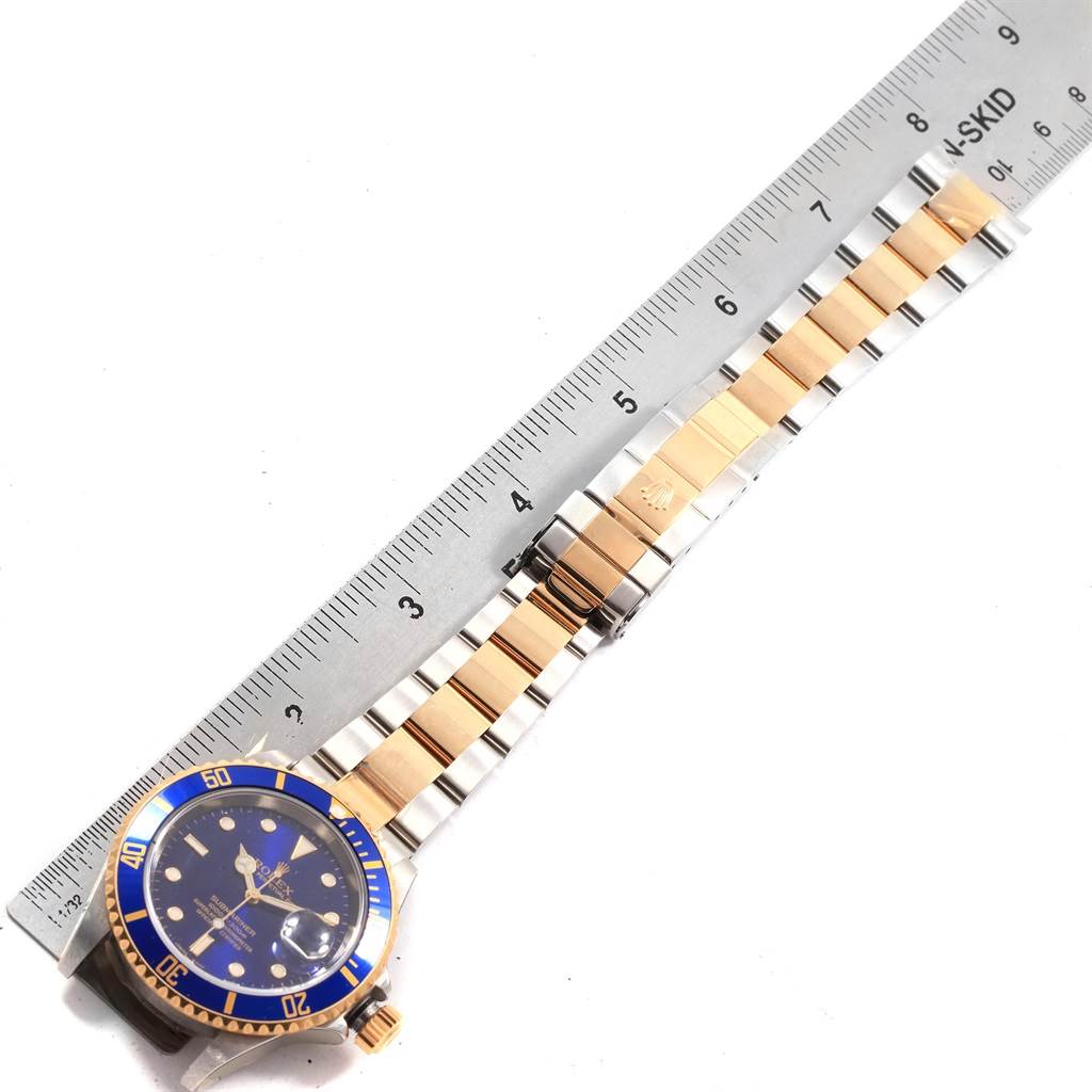 This image shows a Rolex Submariner 16613 Men's Steel and Gold (two tone) Blue Dial 16613 Men's Steel and Gold (two tone) Blue Dial watch laid flat, showcasing the face, bezel, and two-tone bracelet next to a ruler.