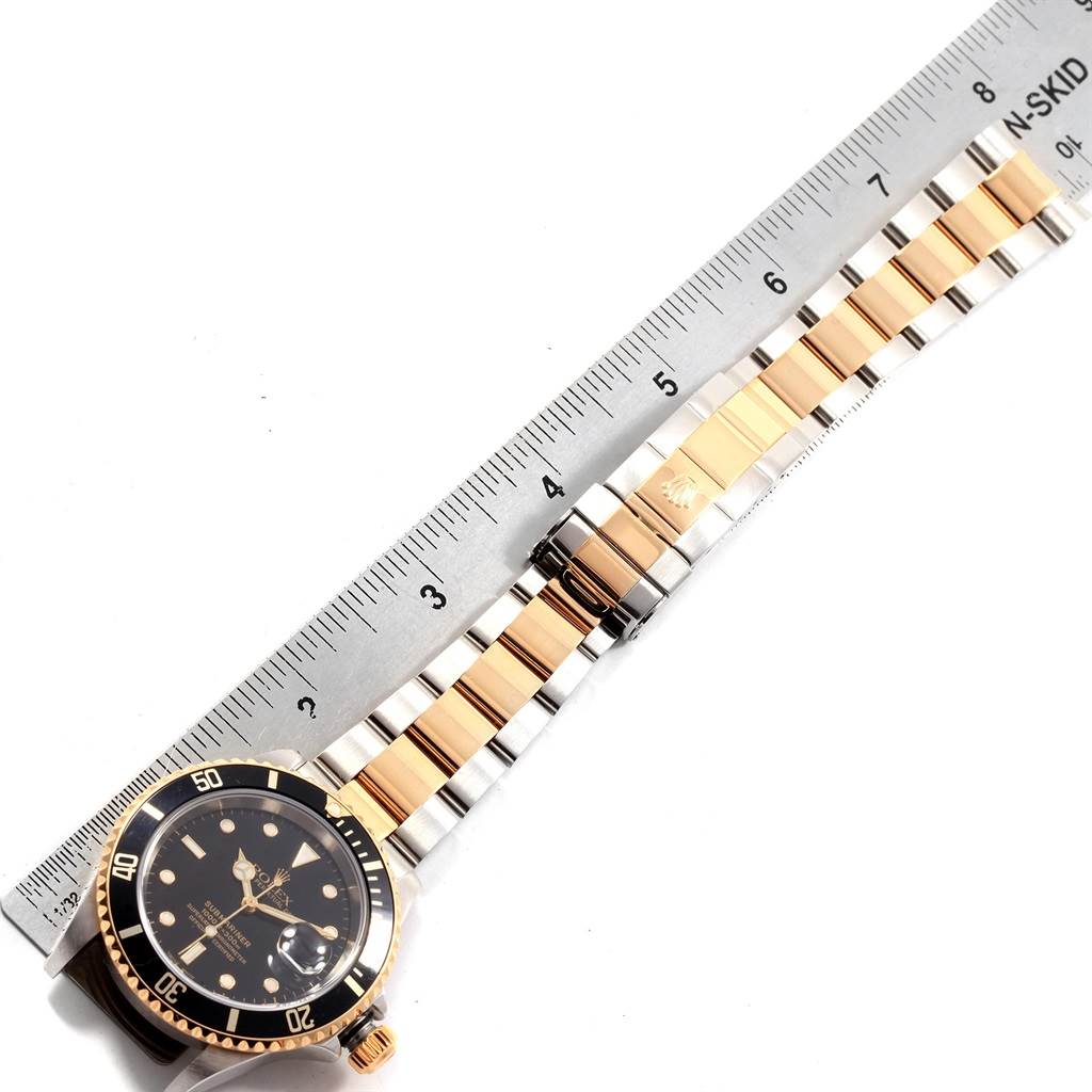 The image shows a Rolex Submariner 16613 Men's Steel and Gold (two tone) Black Dial 16613 Men's Steel and Gold (two tone) Black Dial watch and stainless steel and gold bracelet from an overhead angle, alongside a ruler.