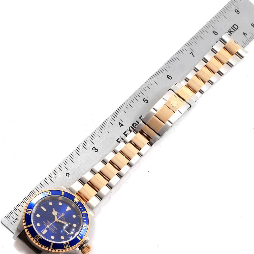 The image shows a Rolex Submariner 16613 Men's Steel and Gold (two tone) Blue Dial 16613 Men's Steel and Gold (two tone) Blue Dial watch laid flat next to a ruler, emphasizing its bracelet and bezel.