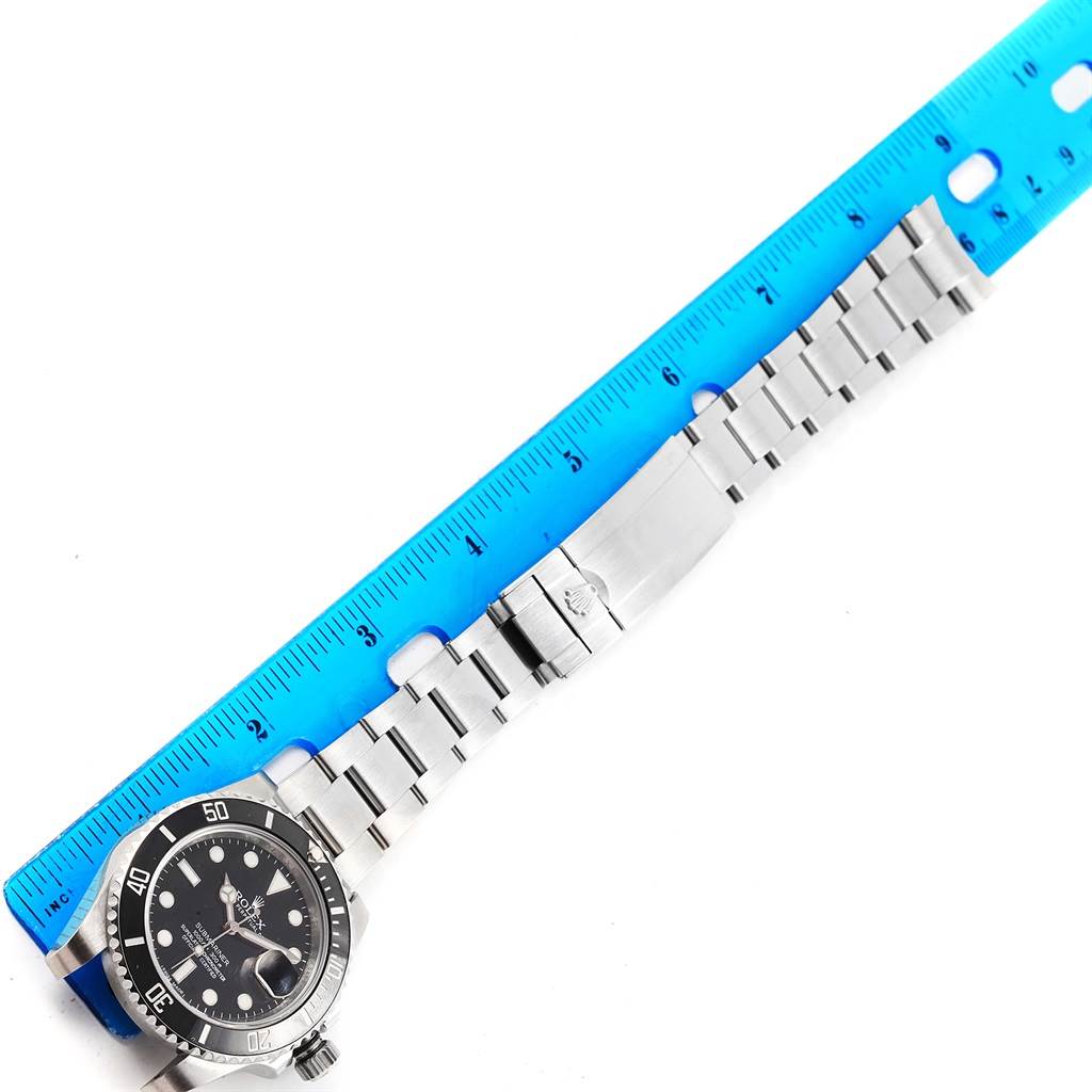 The image shows a Rolex Submariner 116610 Men's Stainless Steel Black Dial 116610 Men's Stainless Steel Black Dial watch and its metal bracelet aligned with a blue ruler, viewed from above.