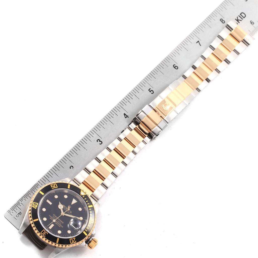 The image shows a top-down view of a Rolex Submariner 16613 Men's Steel and Gold (two tone) Black Dial 16613 Men's Steel and Gold (two tone) Black Dial watch, featuring its case, bezel, dial, and bracelet alongside a ruler.