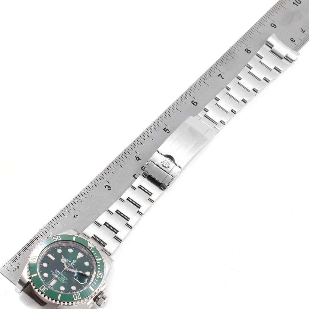 The image shows a Rolex Submariner 116610LV Men's Stainless Steel Green Dial 116610LV Men's Stainless Steel Green Dial watch placed horizontally alongside a ruler, displaying its stainless steel bracelet and green bezel.