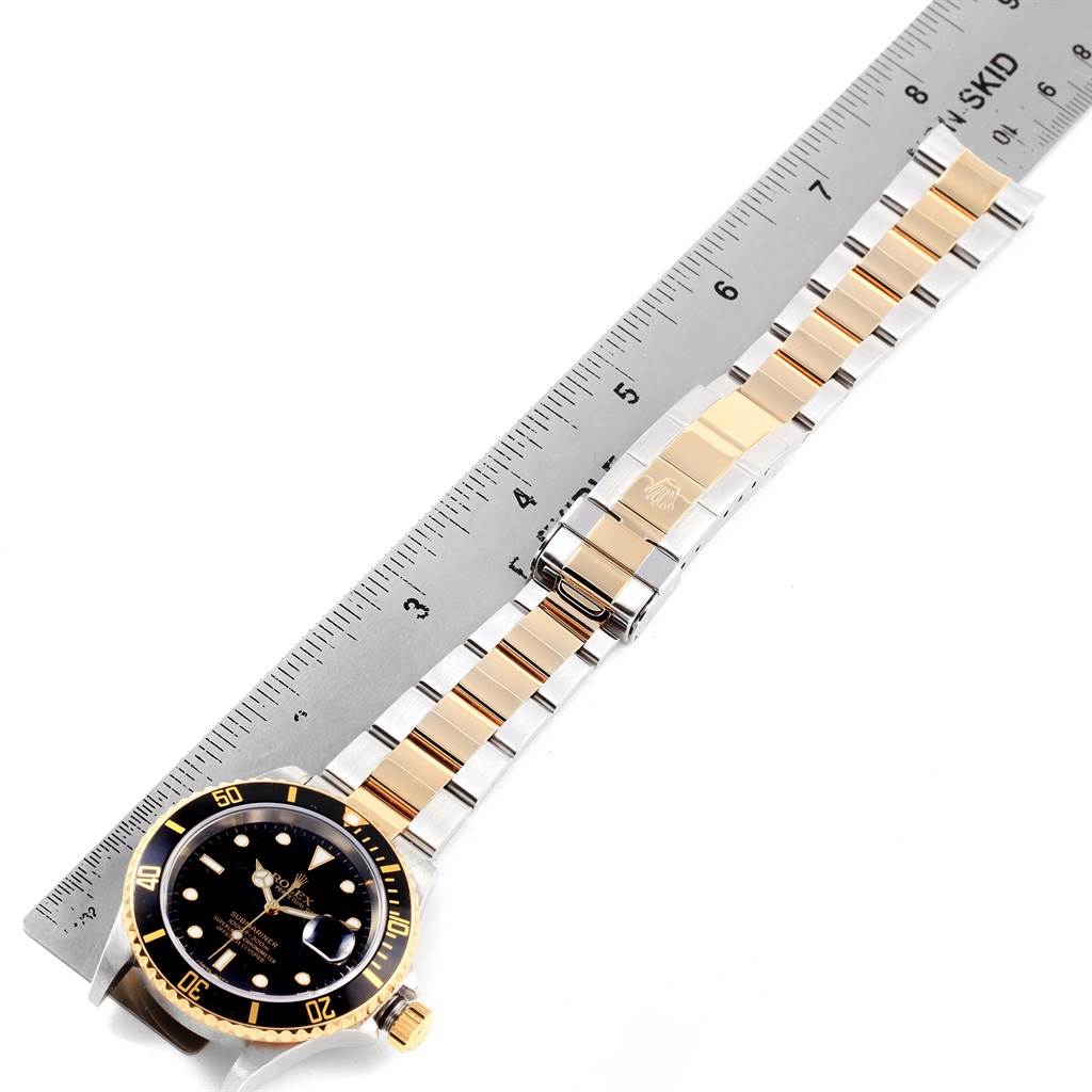 The image shows a top view of a Rolex Submariner 16613 Men's Steel and Gold (two tone) Black Dial 16613 Men's Steel and Gold (two tone) Black Dial watch, displaying the face, bezel, band, and clasp alongside a ruler.