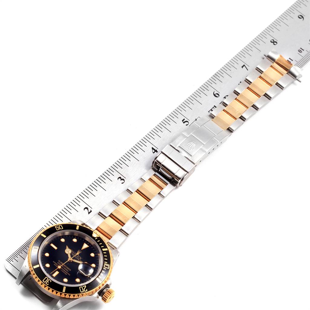 The image shows a Rolex Submariner 16613 Men's Steel and Gold (two tone) Black Dial 16613 Men's Steel and Gold (two tone) Black Dial watch laid flat, displaying its face, bezel, and strap against a ruler.