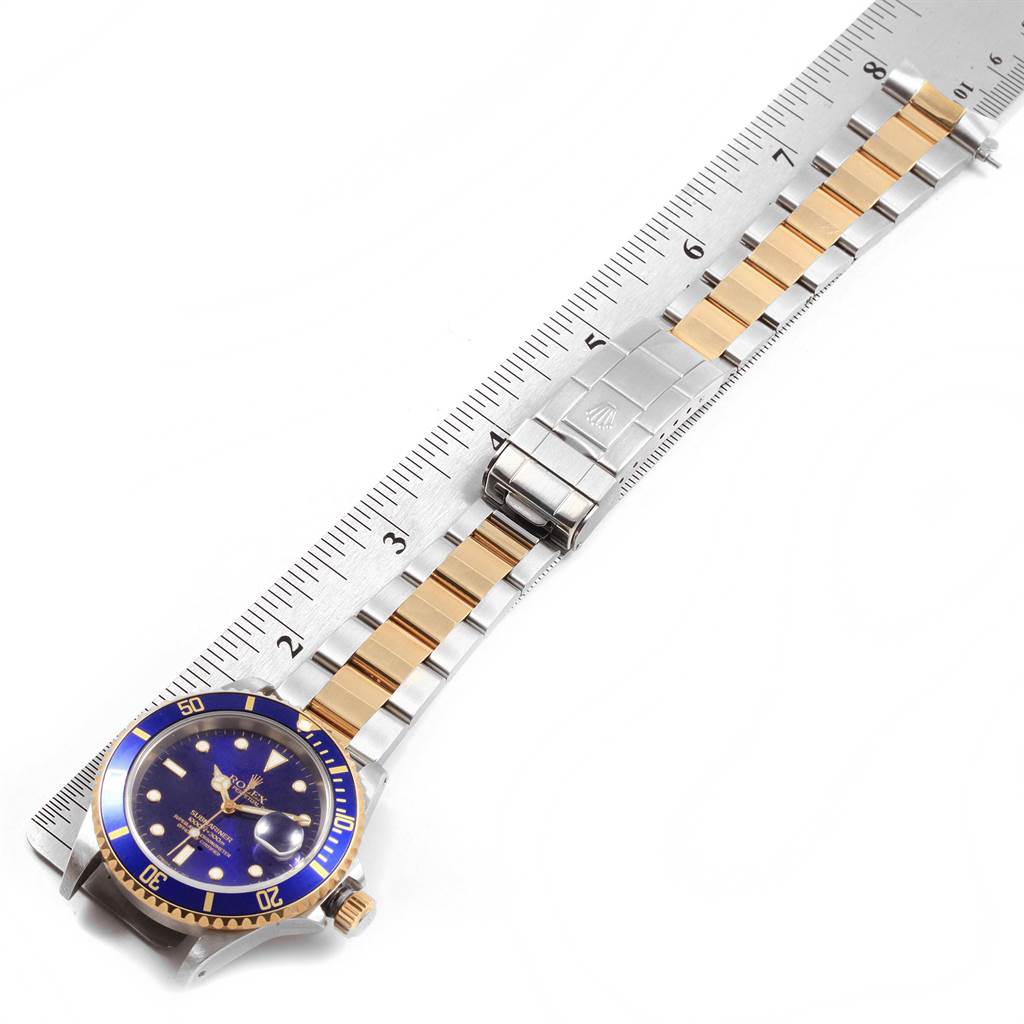 The image shows a Rolex Submariner 16613 Men's Steel and Gold (two tone) Blue Dial 16613 Men's Steel and Gold (two tone) Blue Dial watch laid flat with its strap extended alongside a ruler.