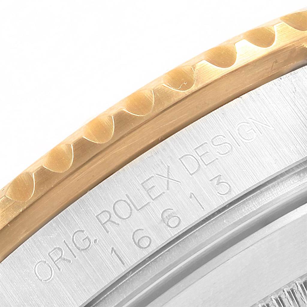 The image shows a close-up of the Rolex logo and model number engraved on the casing edge of a Rolex Submariner 16613 Men's Steel and Gold (two tone) Blue Dial 16613 Men's Steel and Gold (two tone) Blue Dial watch.